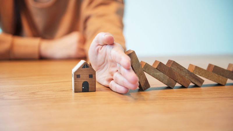 Person putting out their hand to stop dominoes toppling onto a small wooden house